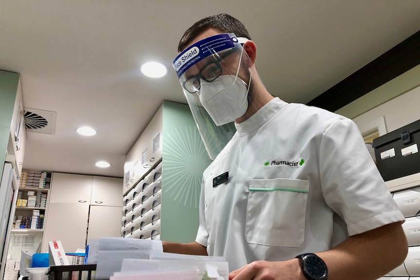 A man in a face shield looks over medical papers.