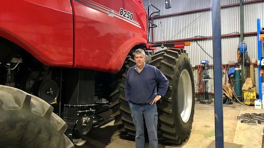 A man in a blue jumper stands beside a red farm machine