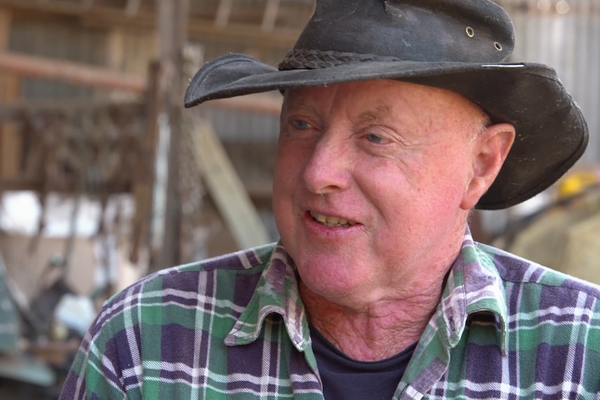 Close up of male face smiling wearing a check shirt and farming hat. 