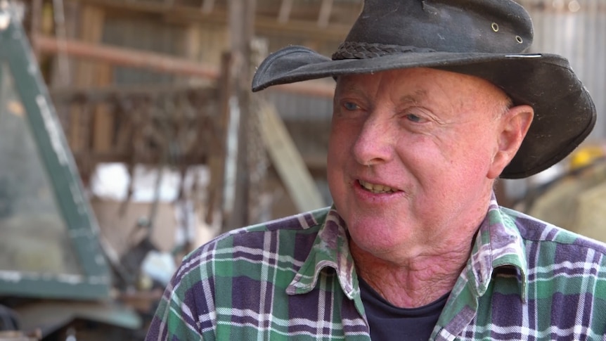 Close up of male face smiling wearing a check shirt and farming hat. 