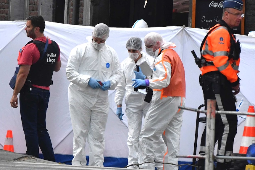 People wearing white uniforms and masks inspect a site.