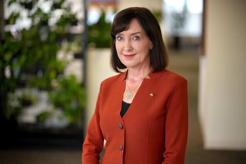 A woman with short brown hair and an orange blazer looking at camera