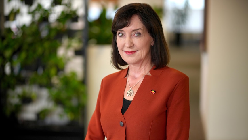 A woman with short brown hair and an orange blazer looking at camera