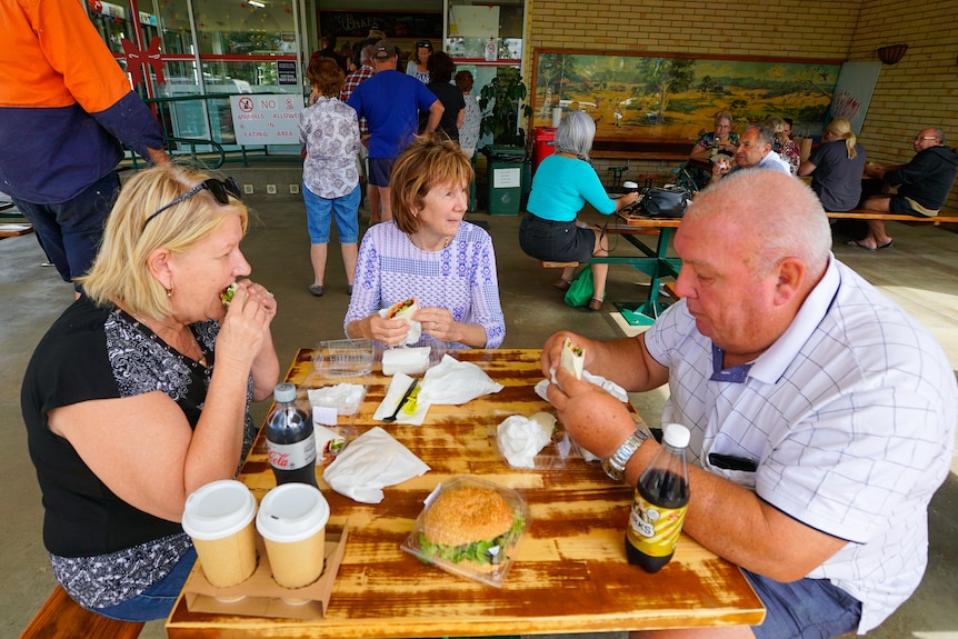 Customers line up at the Gin Gin Bakery as others sit outside eating at tables. 