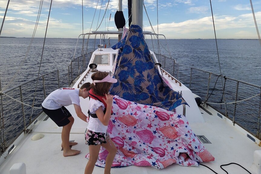 A boy and a girl create a cubby from blankets on the deck of a sailing boat.