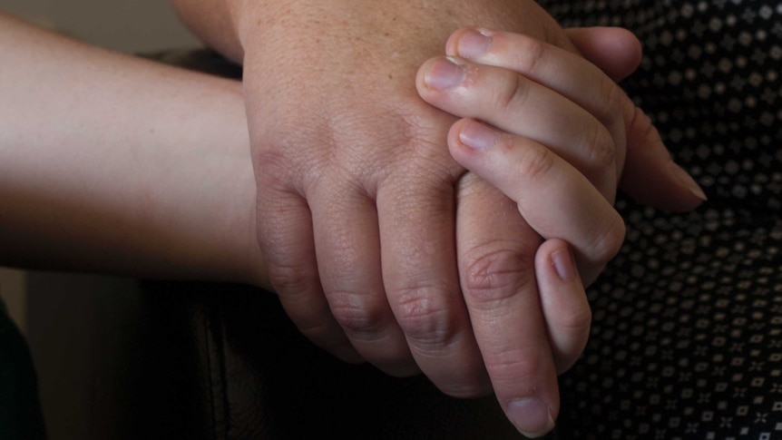 A girl holds her mother's hand.