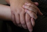 A girl holds her mother's hand.
