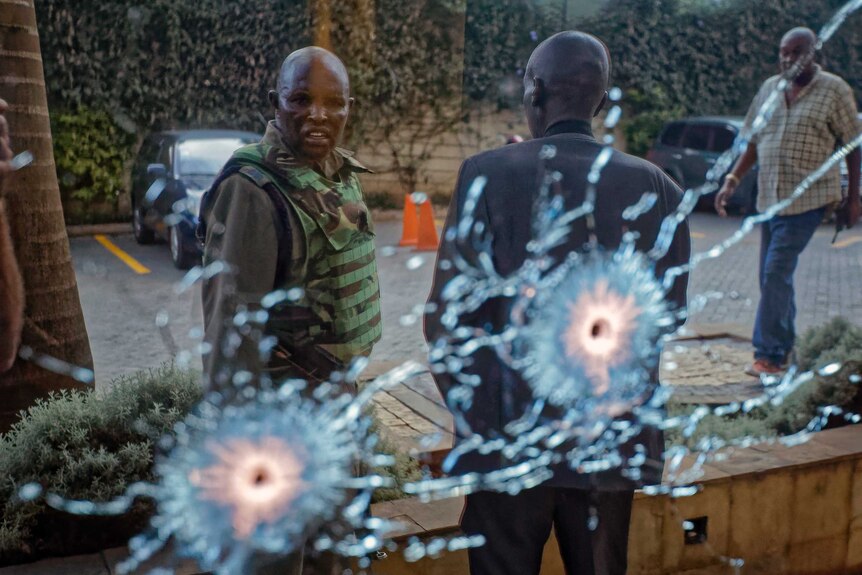 A member of the security forces is seen reflected in a window as he looks at bullet-holes.
