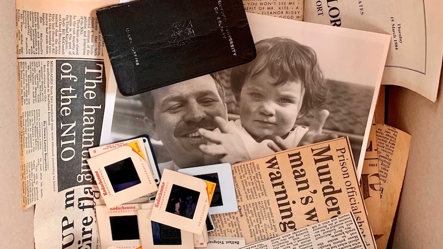 A bird's eye view shows a box of newspaper clippings, a songbook, photographs, film slides, and a passport.