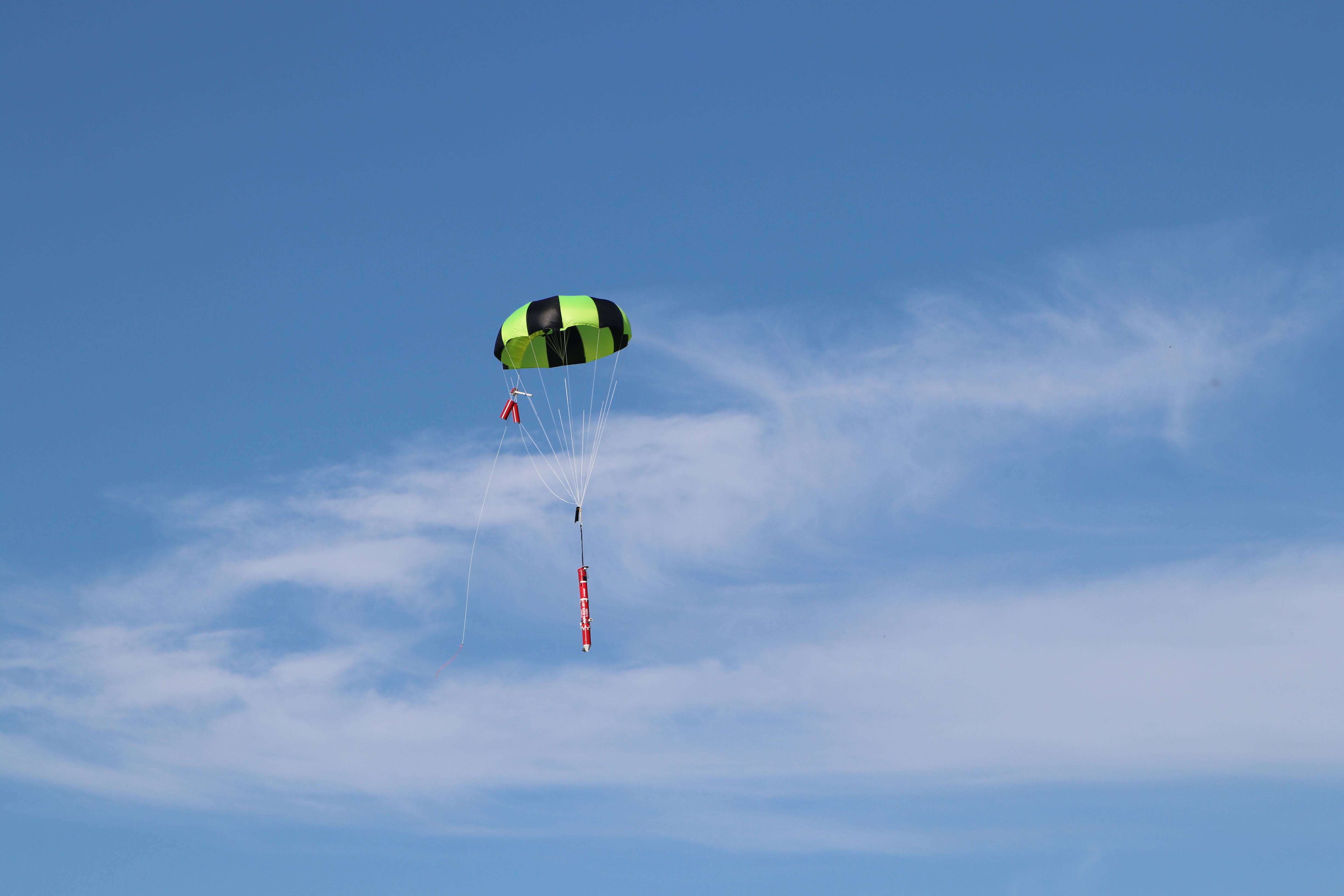 A red device attached to a small parachute in the air.