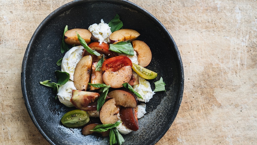 A bowl of caprese salad with wedges of chopped tomato and plum, mozzarella and basil, a fresh recipe for hot days.