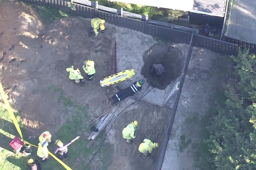 An aerial shot showing a person down a hole with firefighters surrounding the hole.