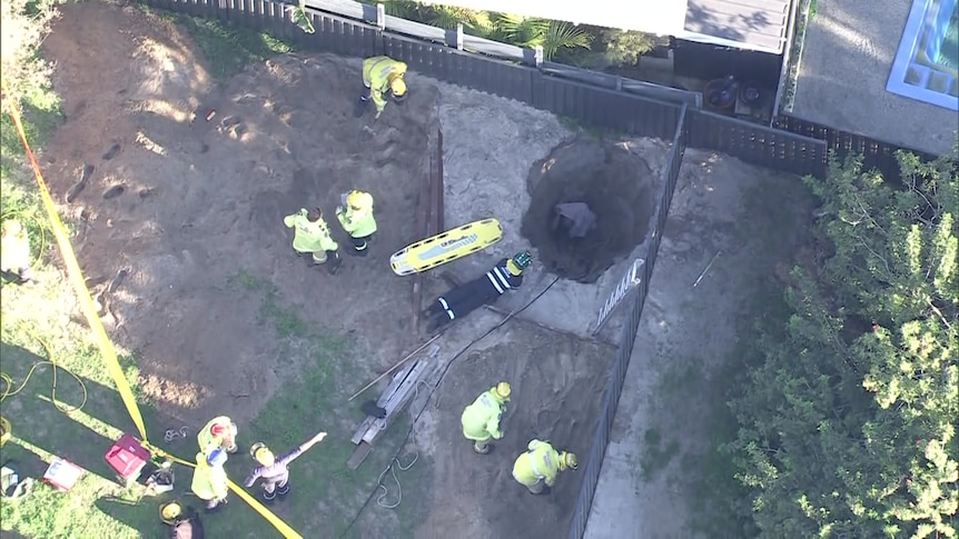 An aerial shot showing a person down a hole with firefighters surrounding the hole.