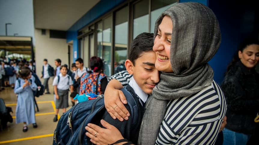 A mother wearing a grey head covering hugs her child, other school chlidren are seen walking behind them.