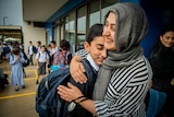 A mother wearing a grey head covering hugs her child, other school chlidren are seen walking behind them.