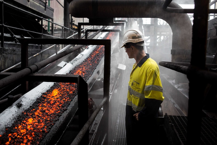 A man in safety gear looks at a conveyor belt of molten ore.