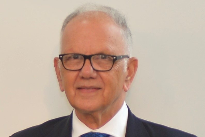 A man with glasses in a suit in front of a beige background