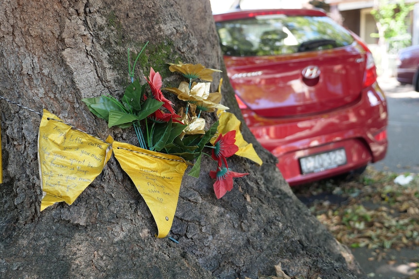 Yellow triangle flags and flowers pinned to a tree trunk on a suburban street