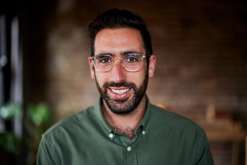 Dr Zac Seidler wearing reading glasses, a green shirt and with a moustache and beard, brown hair