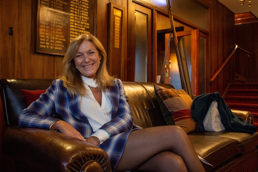 A woman sits on a leather coach smiling at the camera