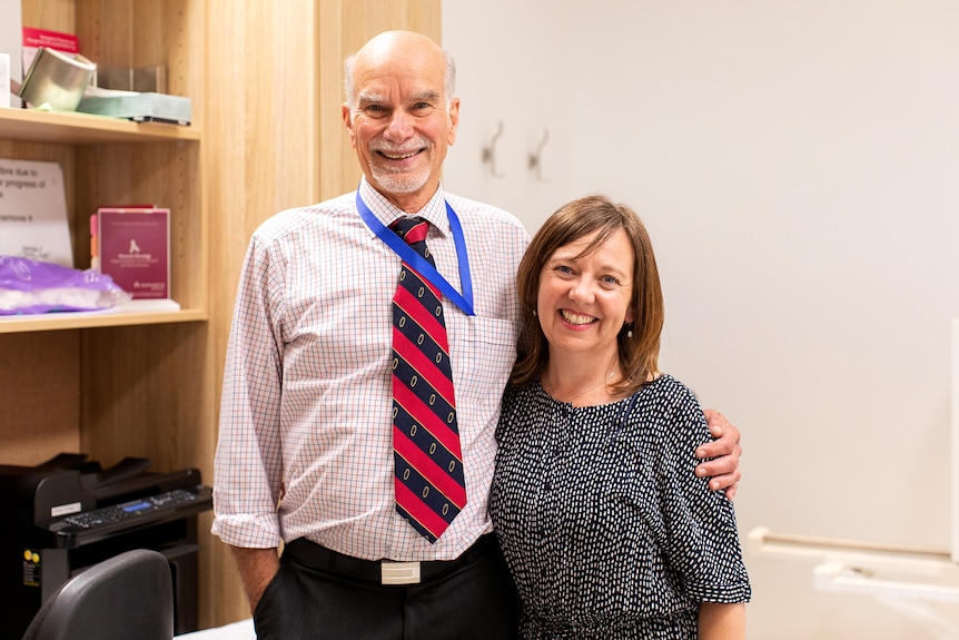 A man and woman stand smiling at a camera