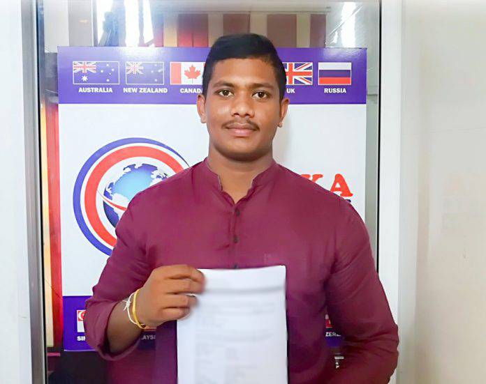 A man wearing a red button up shirt holds a white piece of paper while smiling