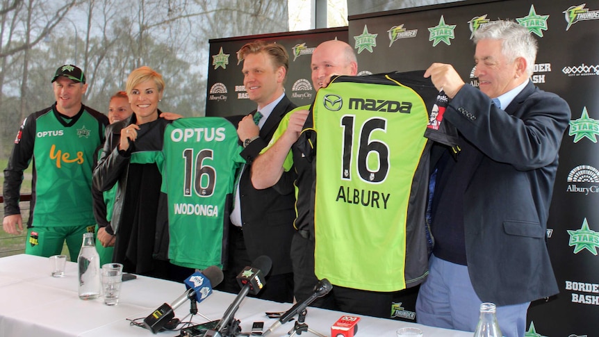 Six people stand in a line holding up two cricket shirts from each team playing at the Border Big Bash.