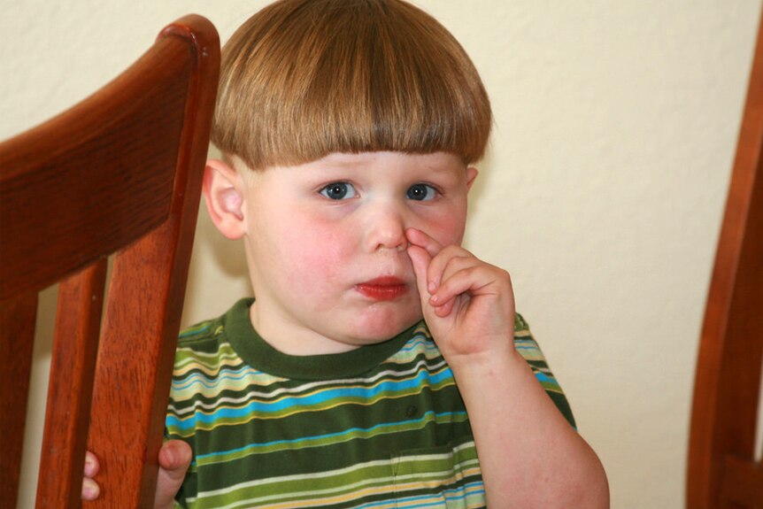 A child with a bad haircut picks his nose.