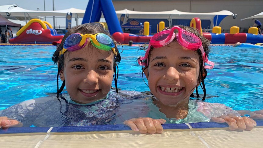 Two girls smile as they hold on to the edge of a pool.