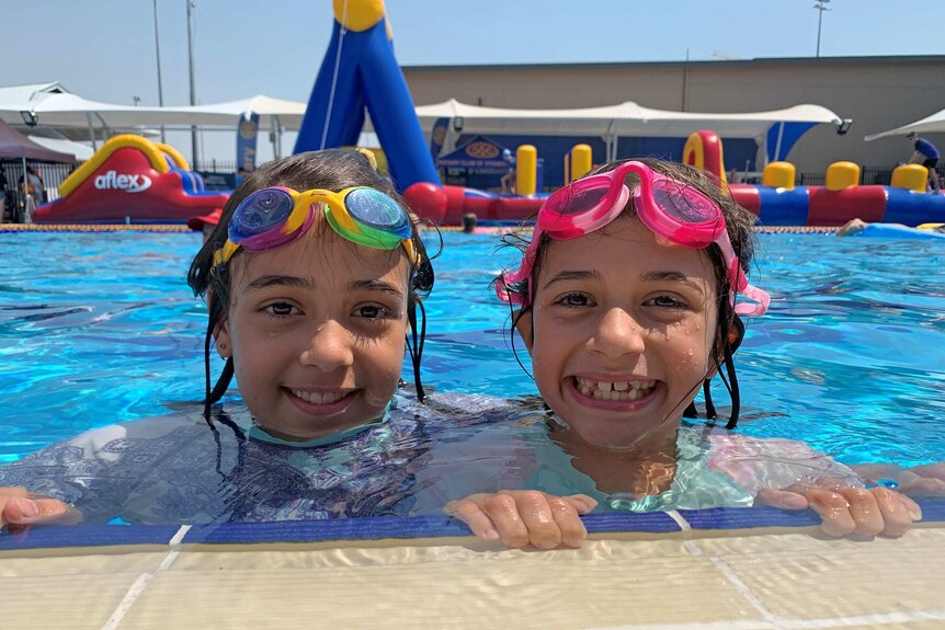 Two girls smile as they hold on to the edge of a pool.
