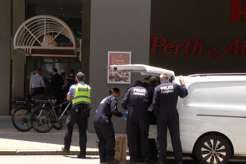 Police officers looking into the boot of a white vehicle outside a hotel 