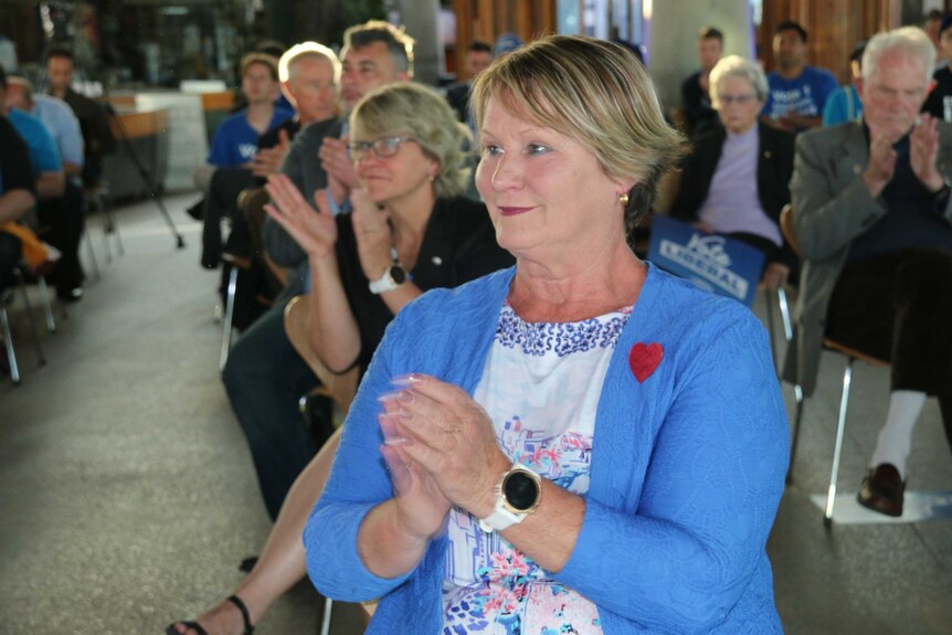 A woman in a blue jacket claps.