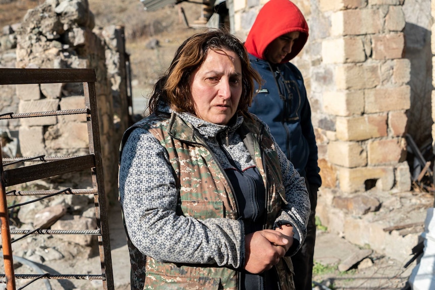 A woman with a worried expression stands in a destroyed building