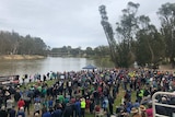 thousands of people stand along the banks of the Murray River