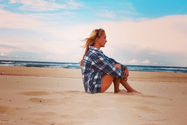 girl with long blonde hair sits in checked shirt on the beach