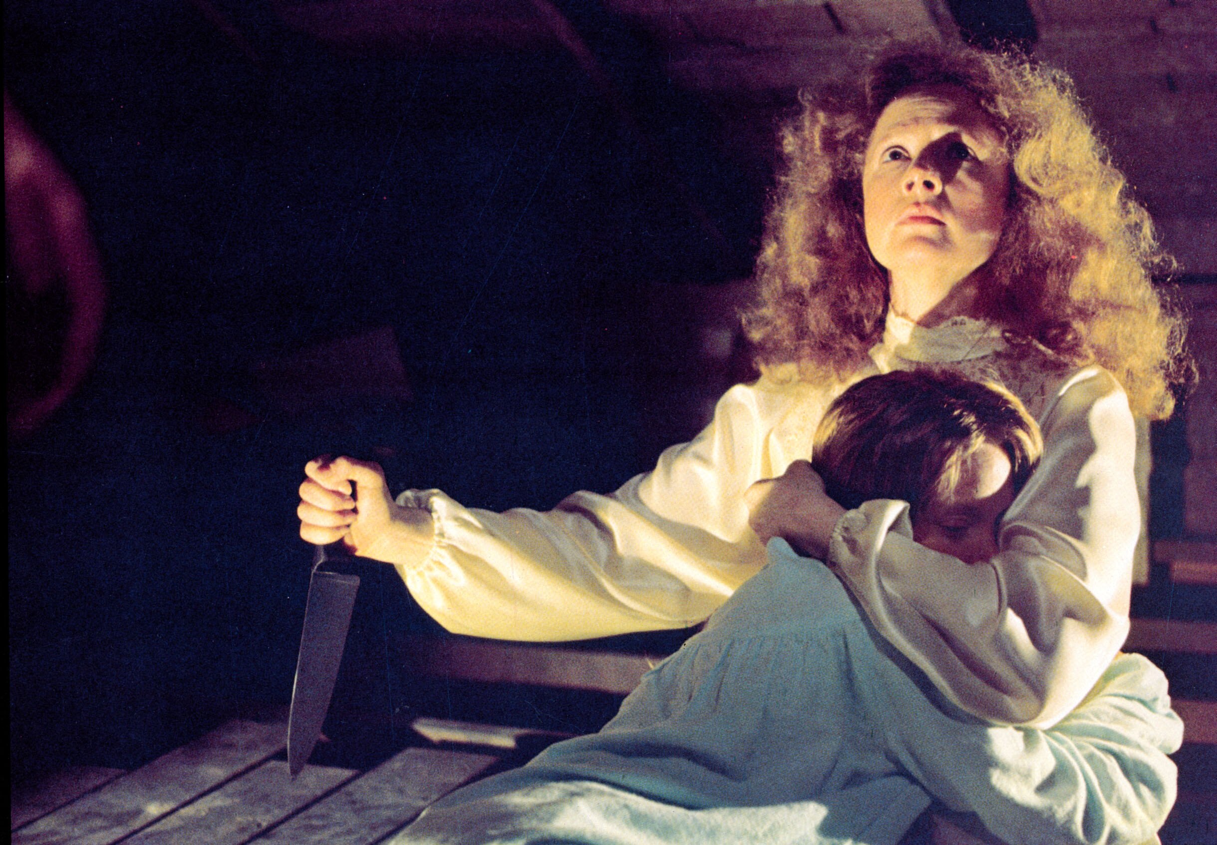 Piper Laurie holds Sissi Spacek in one hand and a knife in the other while looking up on set of the film Carrie