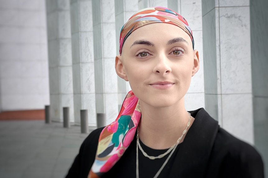 A young woman wearing a patterned bandana standing out the front of parliament, marble pillars visible behind her.