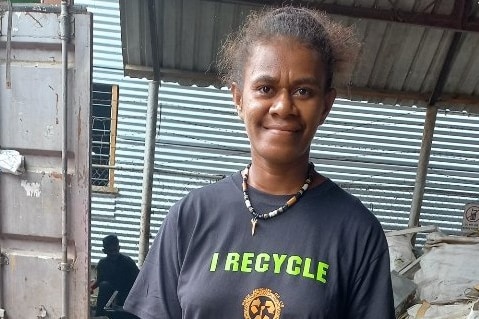 A woman stands outside alongside bags of recycling. 