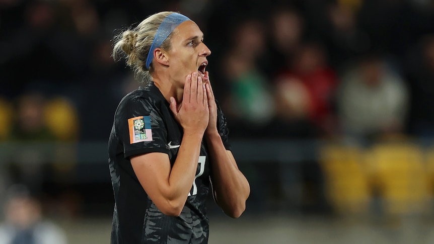 A New Zealand women's footballer reacts in shock with her hands on her face after a goal is disallowed.
