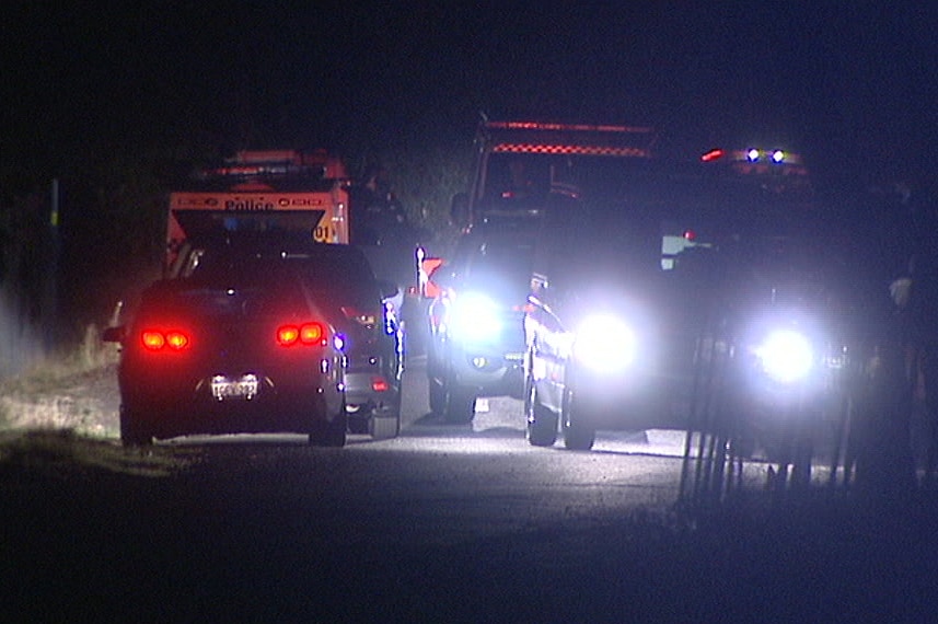 Police cars with their lights on at a rural crime scene at night.