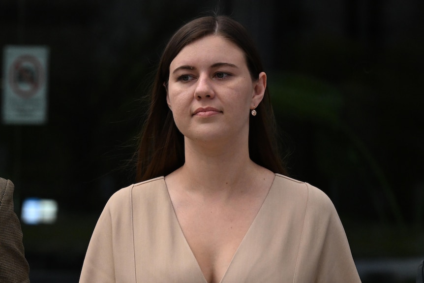 A woman in a tan dress looks serious.