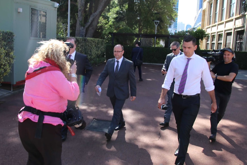 Barry Urban walks through the Parliament House forecourt surrounded by reporters and cameramen.