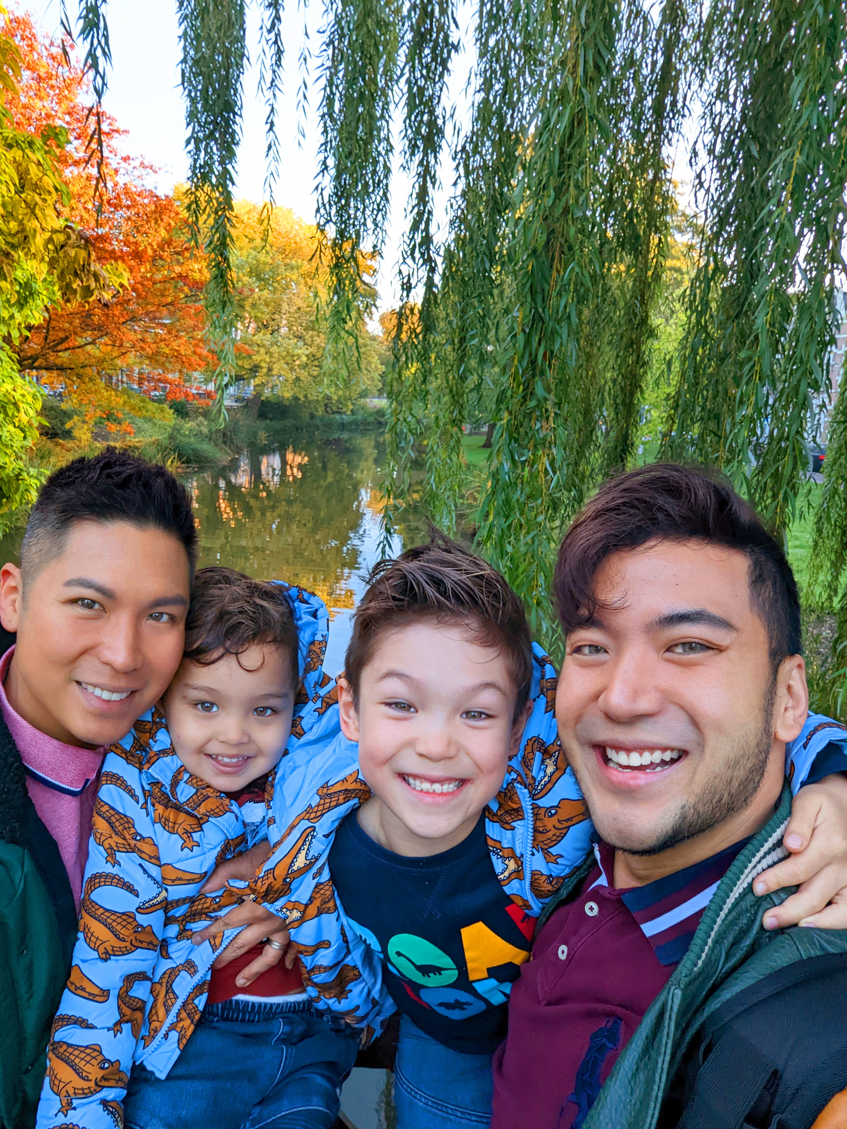 Two dads and two boys pose together with arms around one another smiling, against a forest backdrop.