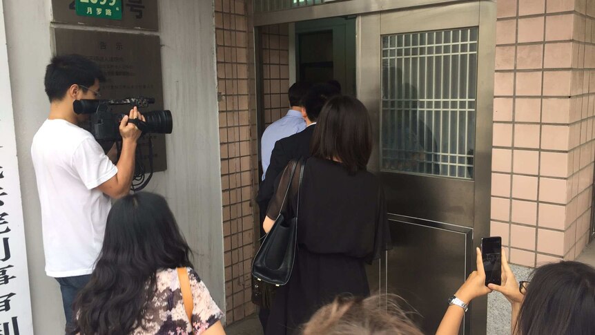 People in suits enter a doorway as members of the media watch on.