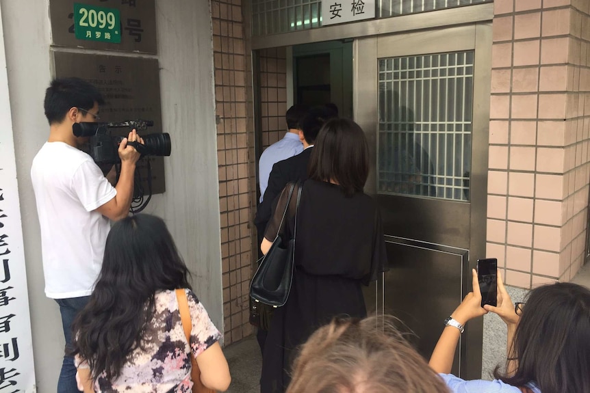 People in suits enter a doorway as members of the media watch on.