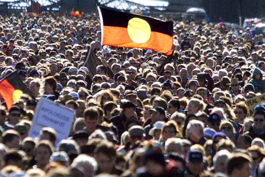 Thousands of people walk across Sydney Harbour Bridge, some holding Aboriginal flags.