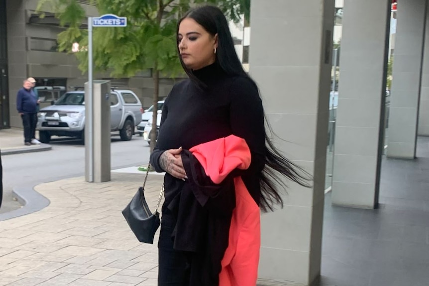 A woman with long black hair walks along a street. 