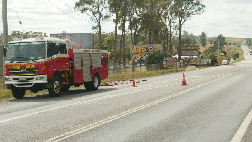 A fire truck is parked on the side of a highway, with two witches hats on the road near it