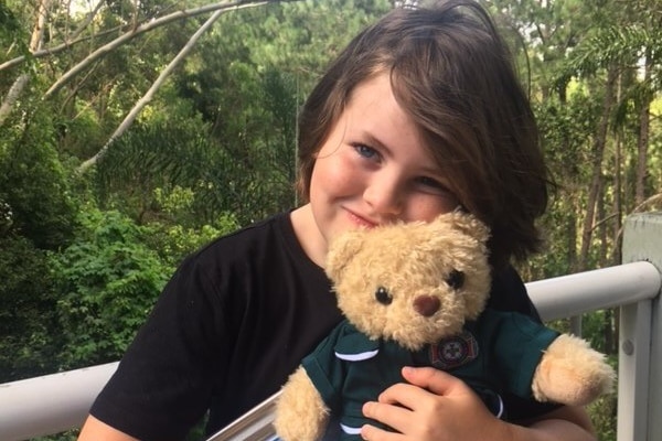 Young boy in a black t-shirt pictured outside, squeezing a teddy-bear