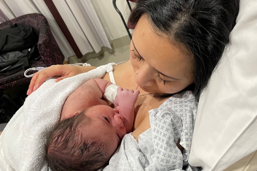 A close up shot of a woman holing and looking at her newborn baby in a hospital bed.